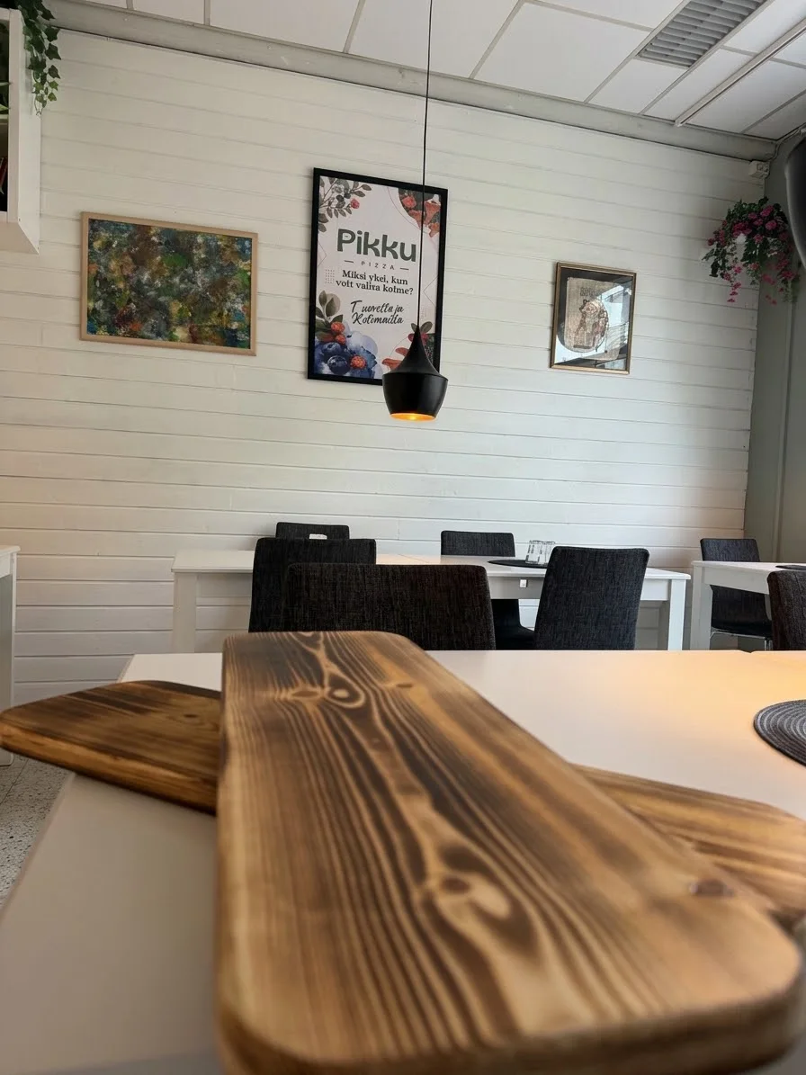 Pikku Pizzan sali — puulaudat pöydällä ja Pikku-juliste seinällä